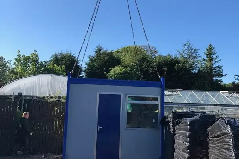 A compact portable cabin being lifted into position over a fence by our HIAB